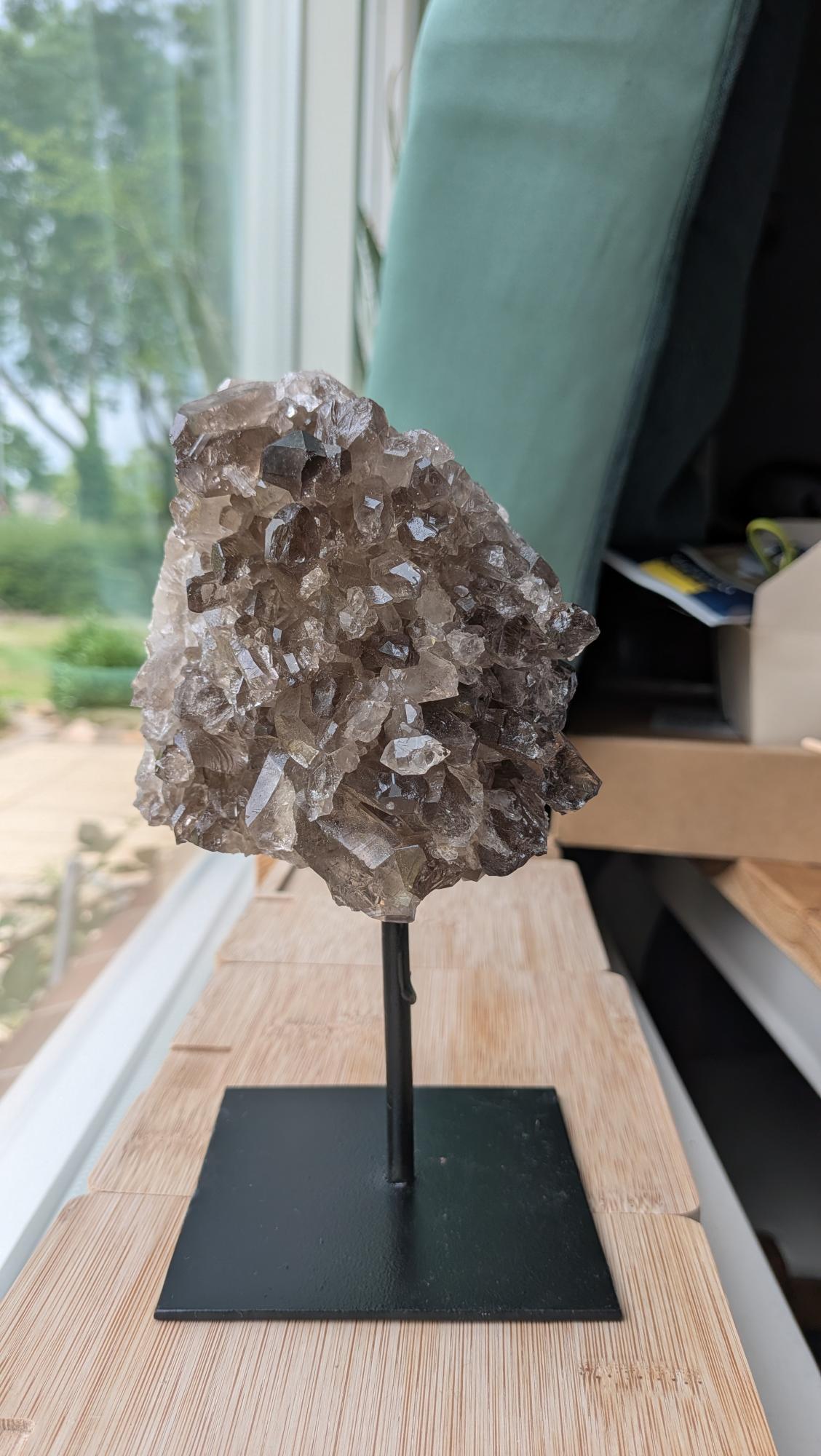 Een rookkwarts cluster van 890 gram op een zwarte standaard, met zicht op de diepe rokerige kristalstructuur