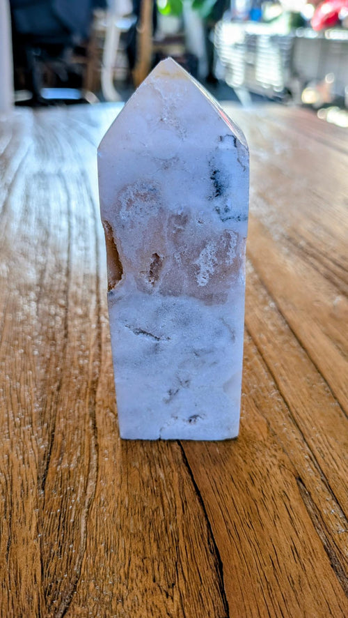 "Gepolijste Roze Amethist tower met Bloemagaat insluitingen op een houten ondergrond, uniek kristal in zachtroze en witte tinten."