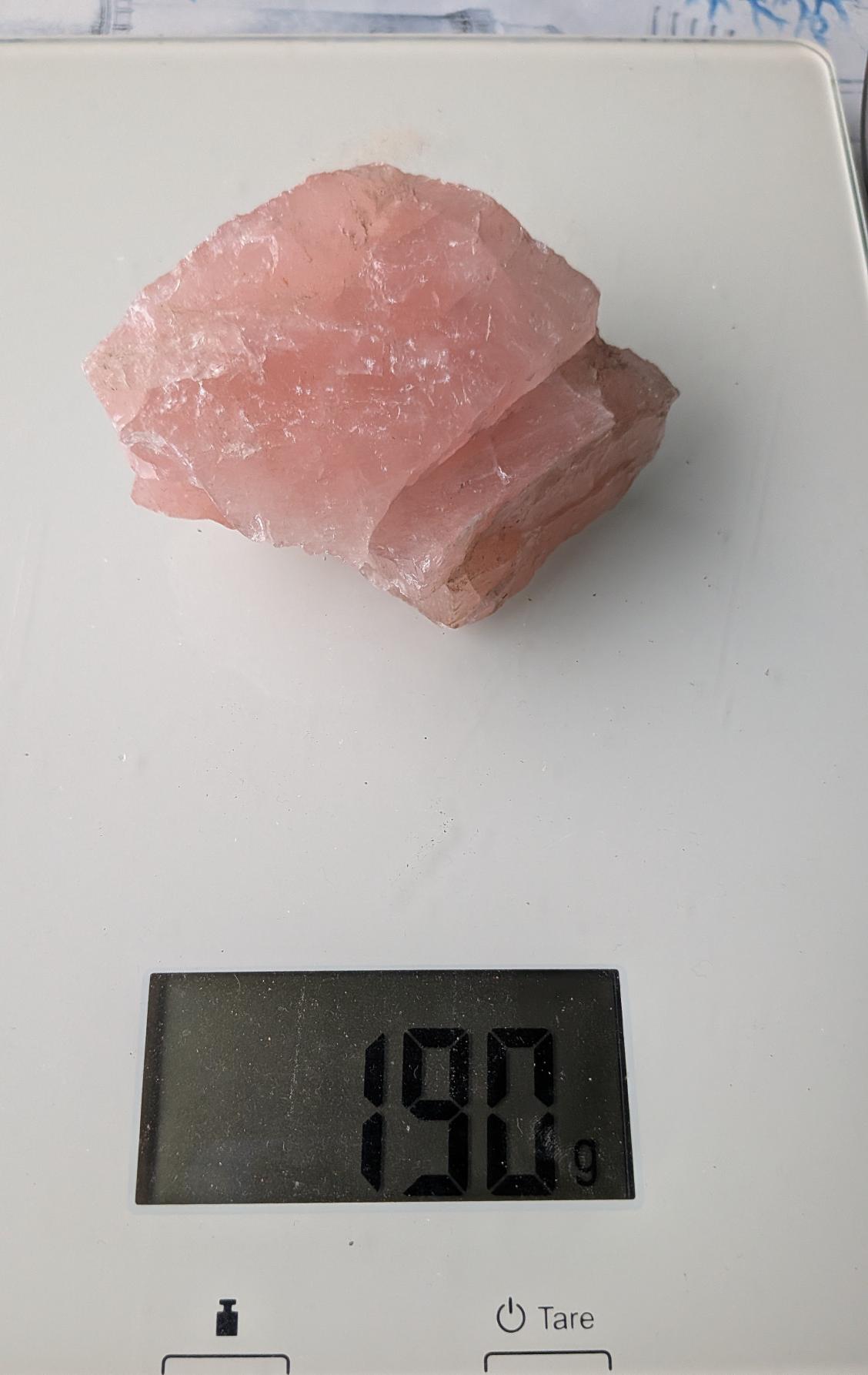 Een mooi, ruw stuk Rozenkwarts van 190 gram met een zachtroze kleur en natuurlijke textuur, gefotografeerd op een digitale weegschaal.