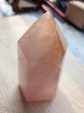 Handgepolijste Rozenkwarts punt kristal tower van 290 gram en 9 cm hoog op een houten ondergrond.