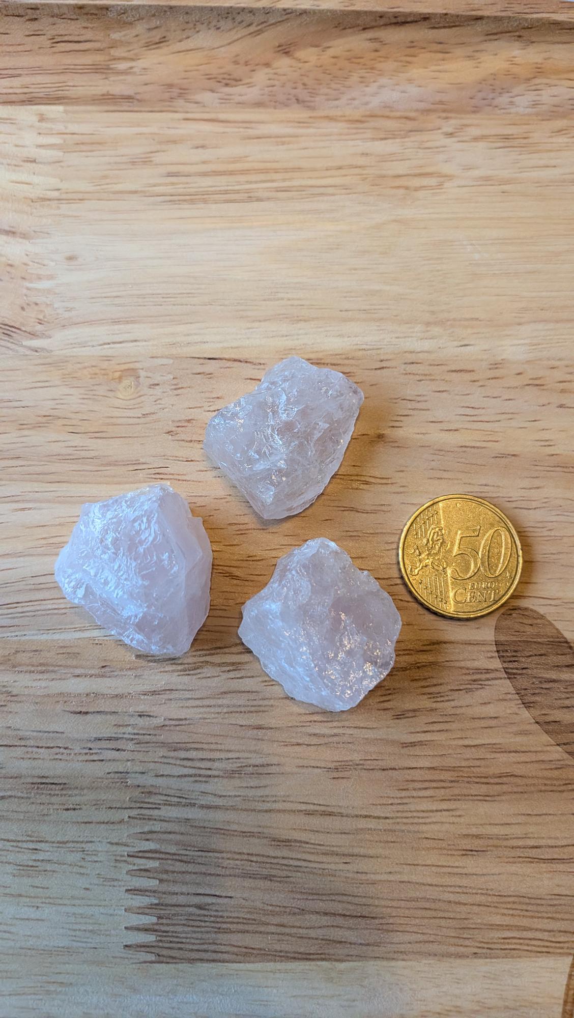 Drie ruwe roze rozenkwarts edelstenen naast een 50 eurocent munt op een houten achtergrond, klaar voor een custom made wire wrapped hanger.