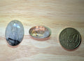 Twee ovale Rutielkwarts edelstenen met gouden en zwarte naaldvormige insluitingen naast een 50 eurocent munt.