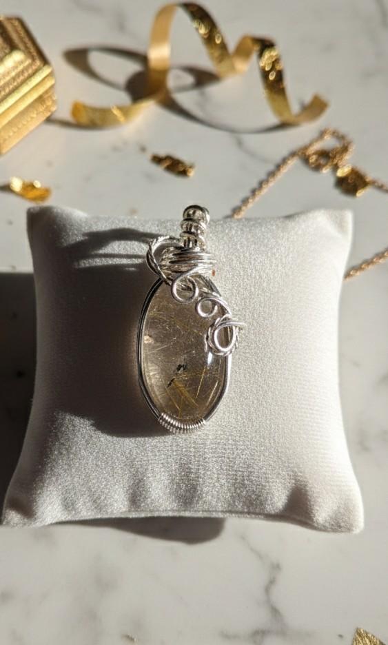 Detailopname van een Goud Rutielkwarts hanger met verzilverde wire wrap en gouden accenten op de achtergrond.
