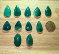 Gefacetteerde groene Serpentijn edelstenen in druppel- en ovaalvorm naast een euromunt ter vergelijking.