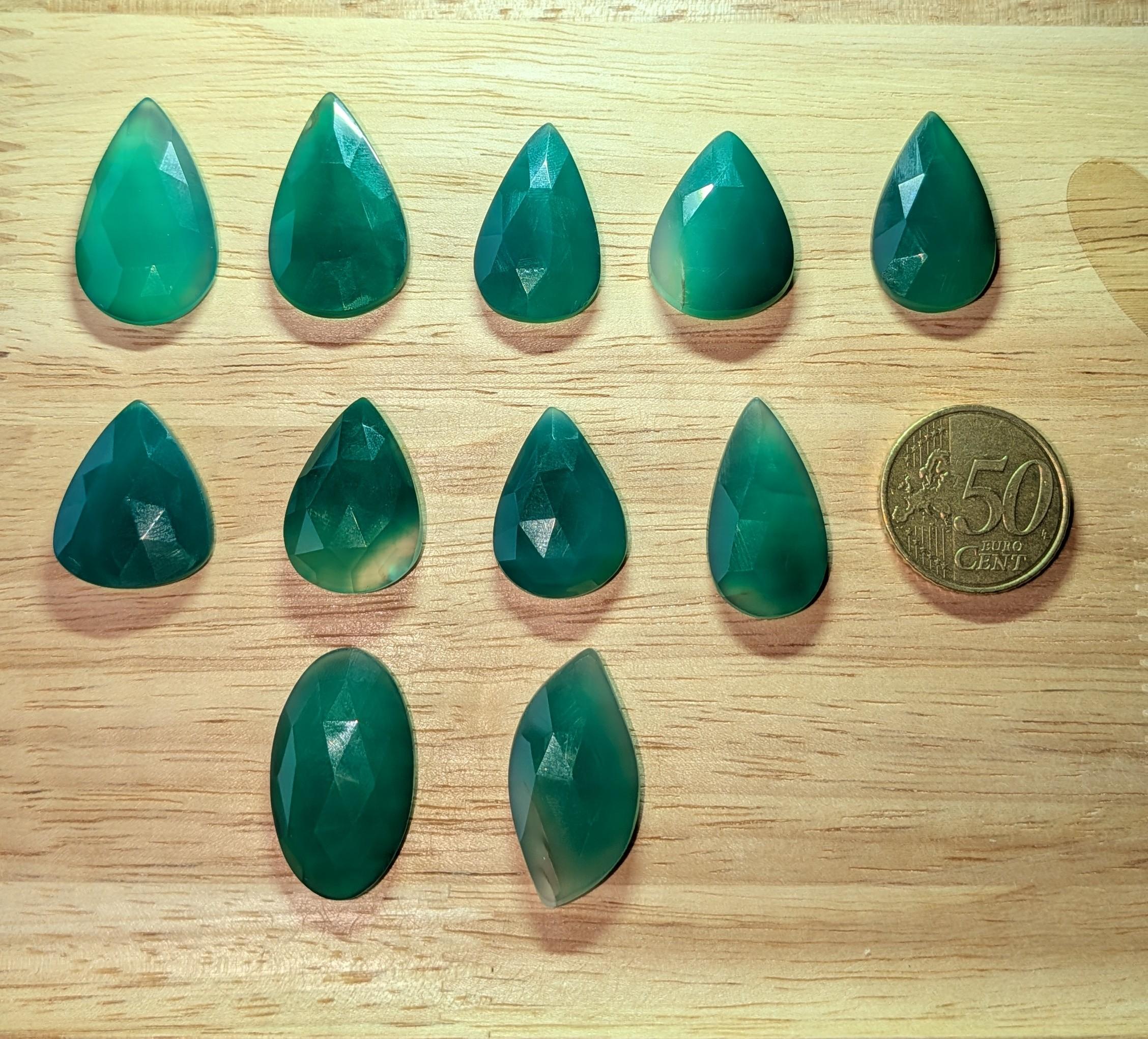 Gefacetteerde groene Serpentijn edelstenen in druppel- en ovaalvorm naast een euromunt ter vergelijking.