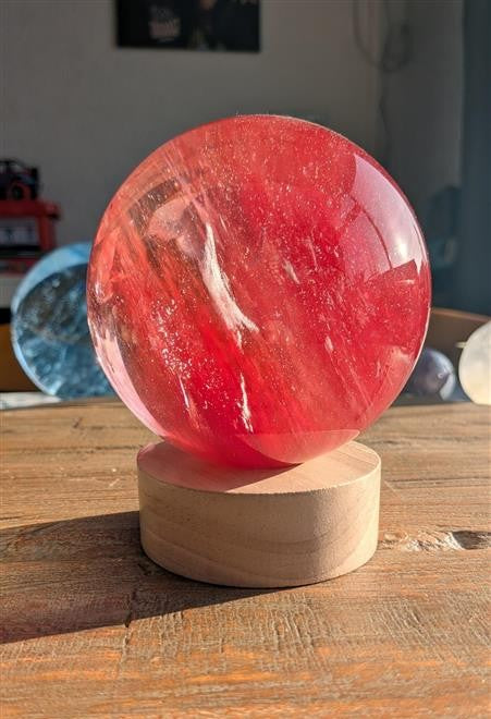 Een massieve, heldere smeltkwarts bol van 10 cm op een ronde houten LED-standaard die de bol van binnenuit verlicht met een warme gloed.