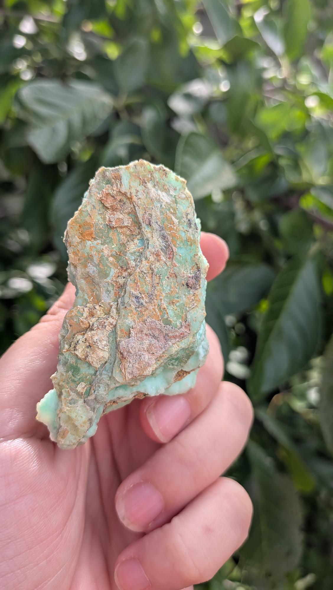 Een hand houdt een gelaagd, mintgroen Smithsoniet-stuk van 84 gram vast, met een robuuste, natuurlijke textuur