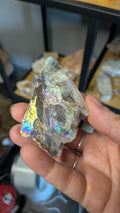 Een hand houdt een aura sphaleriet specimen vast, met een prachtig regenboog-effect.