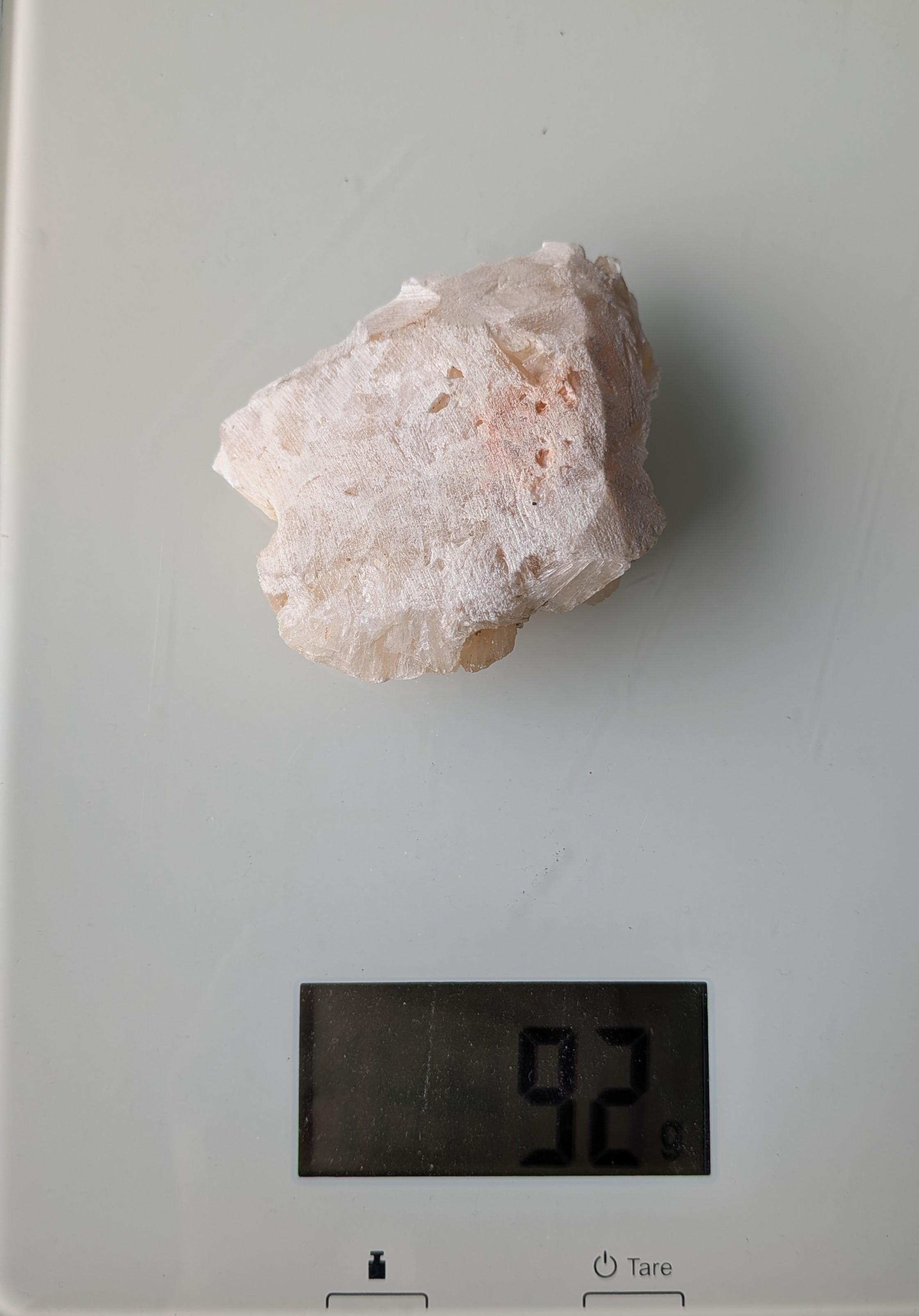 Een natuurlijk, perzikkleurig Stilbiet cluster met waaiervormige kristalstructuren uit Nasik, India, gewogen op een digitale weegschaal die 91 gram aangeeft.