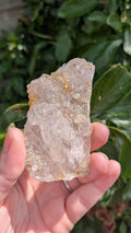 Een hand houdt een sprankelende suiker druzy chalcedoon van 54 gram vast, met een fijne, suikerachtige kristaltextuur