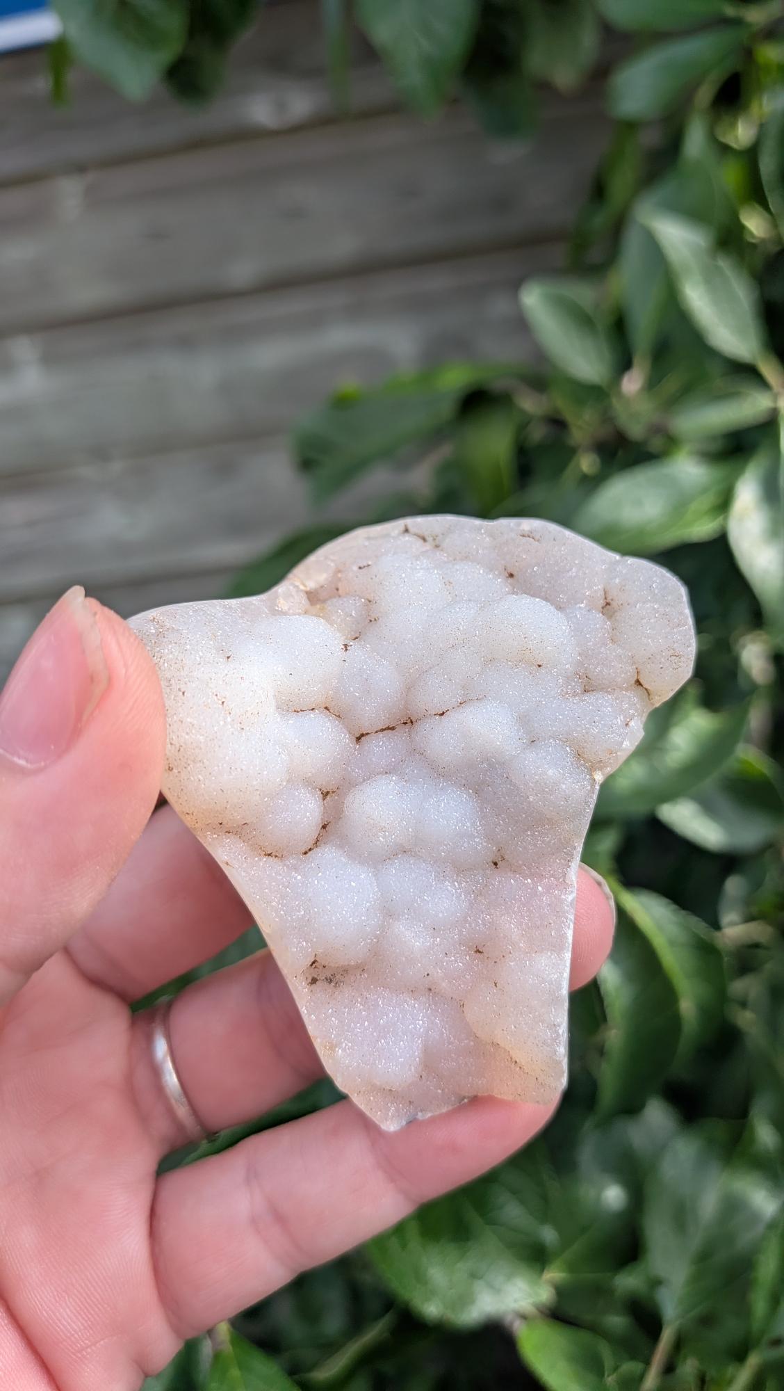 Een hand houdt een sprankelende suiker druzy chalcedoon van 47 gram vast, met een fijne, suikerachtige kristaltextuur