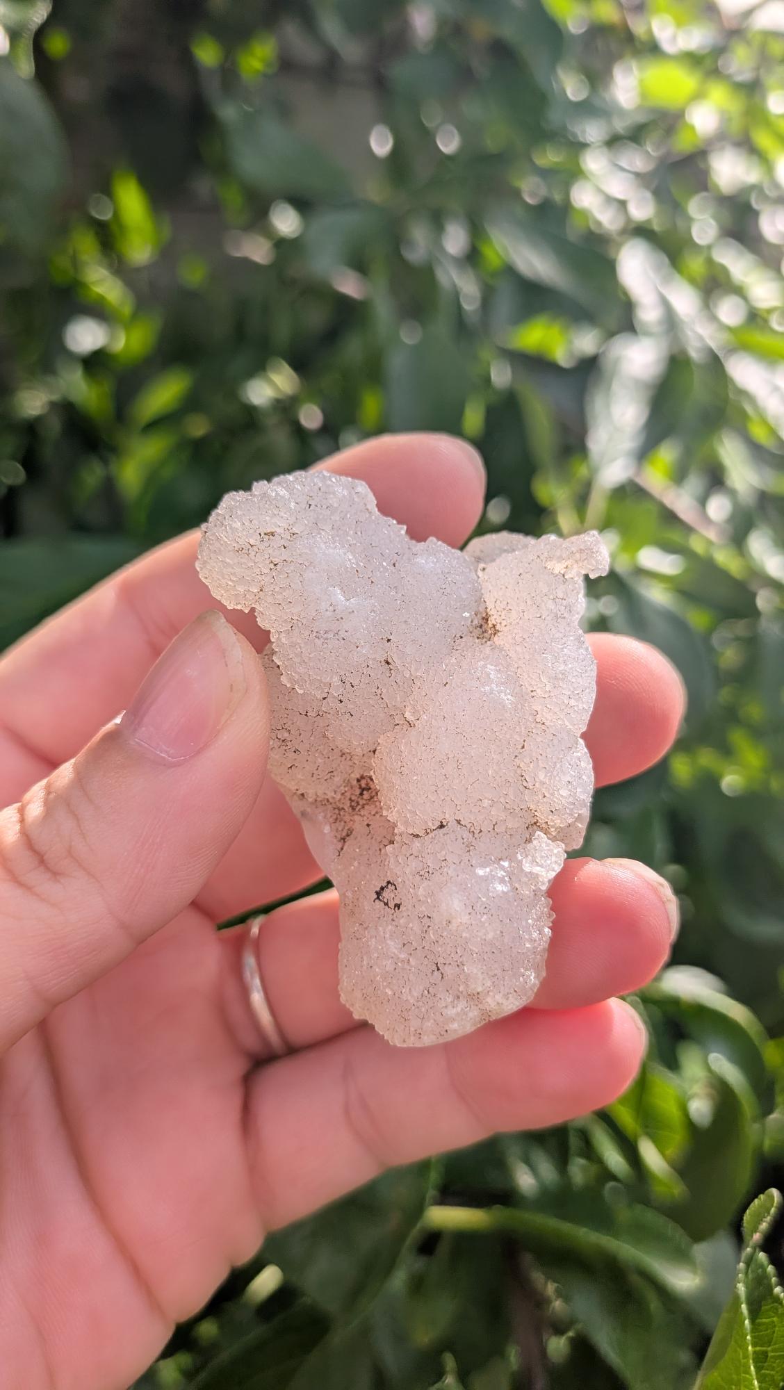 Een hand houdt een sprankelende suiker druzy chalcedoon van 50 gram vast, met een fijne, suikerachtige kristaltextuur