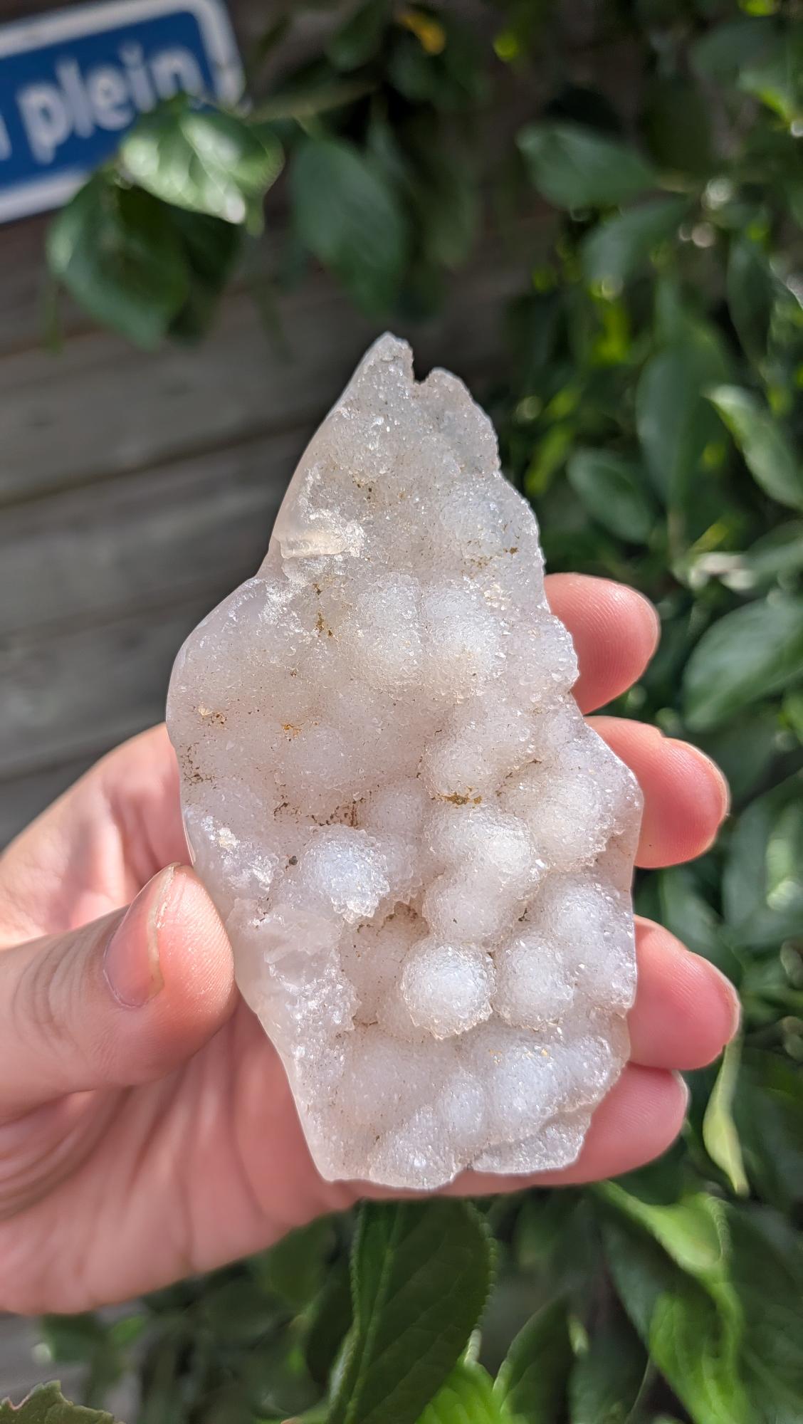 Een hand houdt een sprankelende suiker druzy chalcedoon van 74 gram vast, met een fijne, suikerachtige kristaltextuur