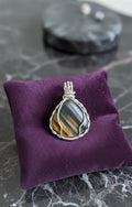 Handgemaakte Tijgeroog hanger gewrapt in verzilverd draad op een luxe kussentje - Edeltwist edelsteen sieraden.