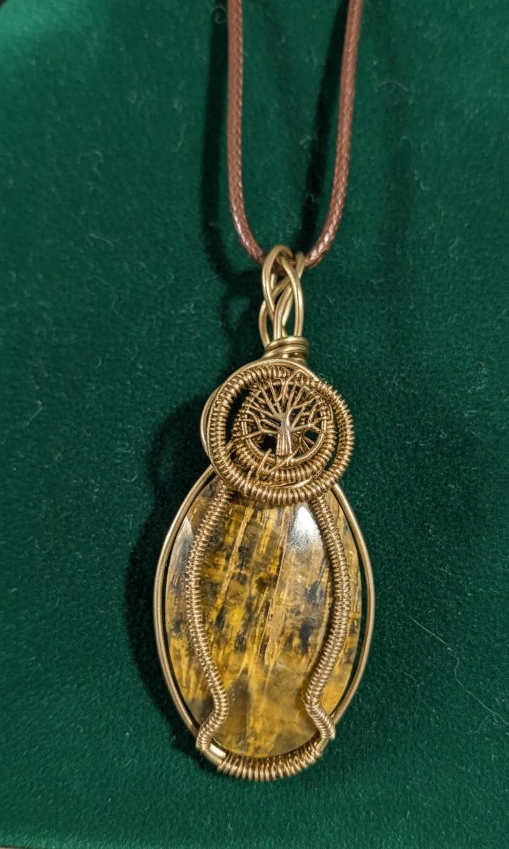 Handgemaakte messing wire-wrap hanger met een ovale tijgeroog edelsteen en een gedetailleerd Tree of Life symbool aan een bruin koord.