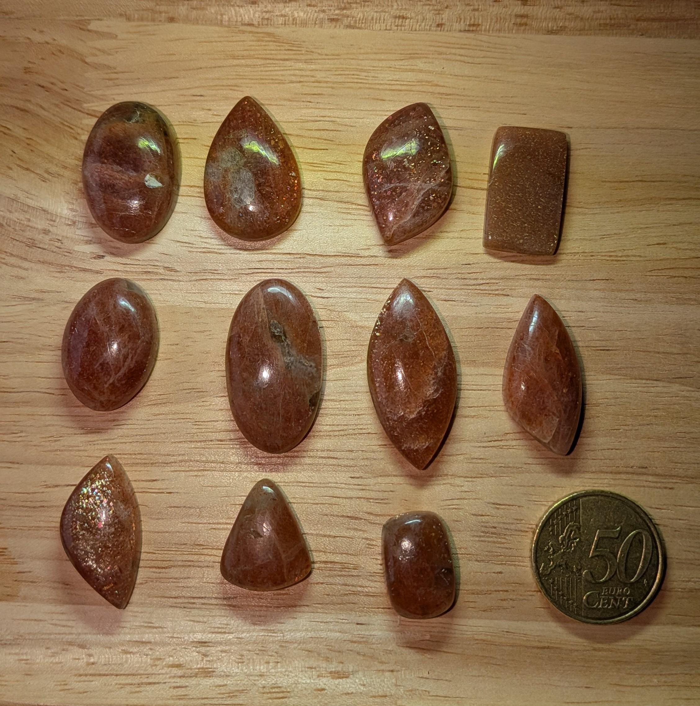 Selectie van elf oranjebruine Zonnesteen edelstenen in diverse vormen (ovaal, druppel, rechthoek, markies) naast een 50 eurocent munt.