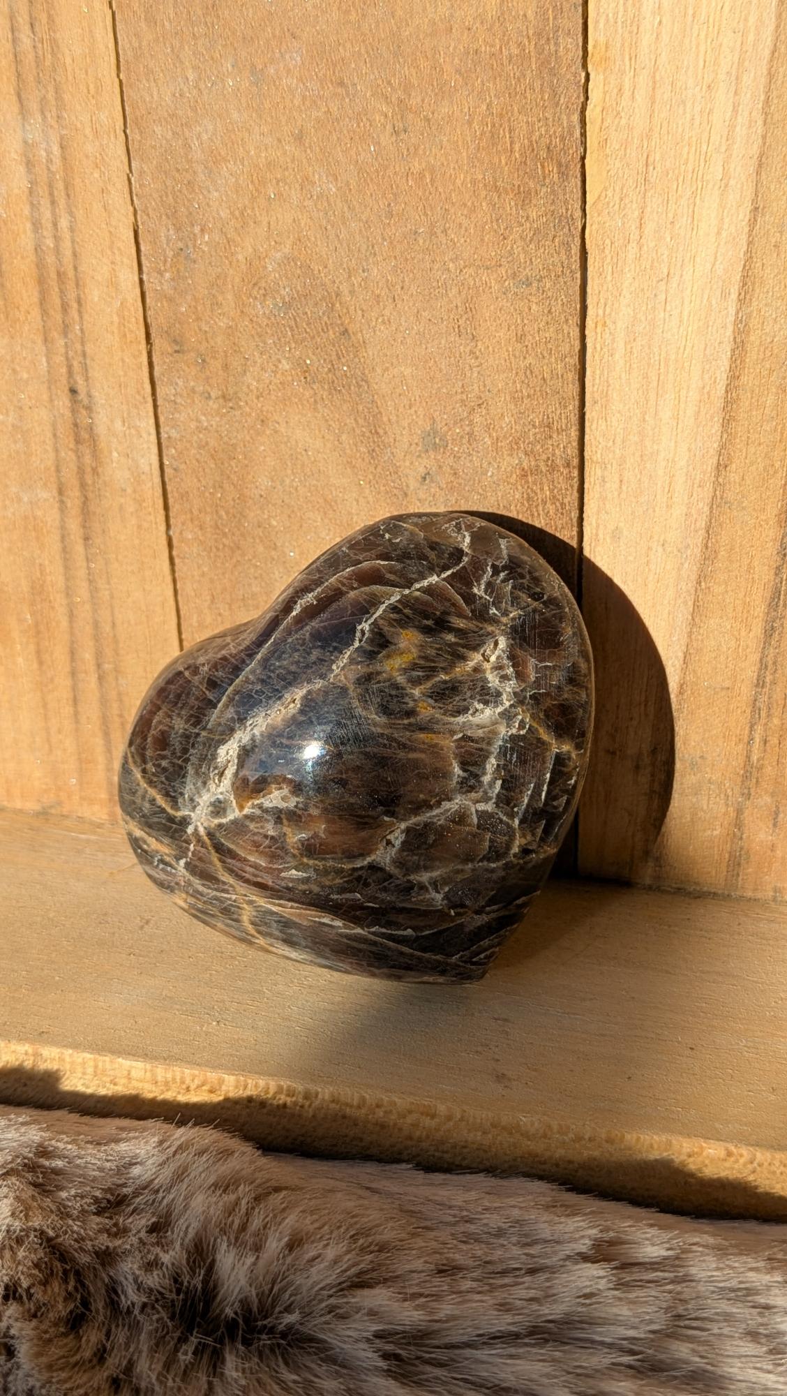Middelmaat edelsteen hart van zwarte maansteen met goudbruine glans en aderingen op een houten achtergrond