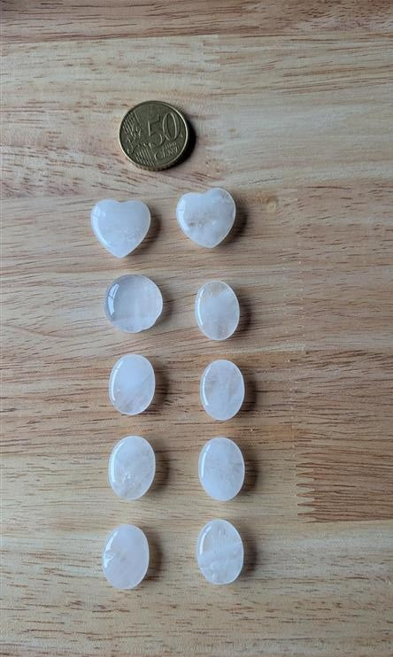 Tien gepolijste bergkristal edelstenen, waaronder twee hartjes en meerdere ovalen, naast een 50 eurocent munt op een houten ondergrond.