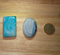 Twee gepolijste Blauwe Chalcedoon edelstenen (rechthoek en ovaal) met witgestreepte patronen naast een 50 eurocent munt.