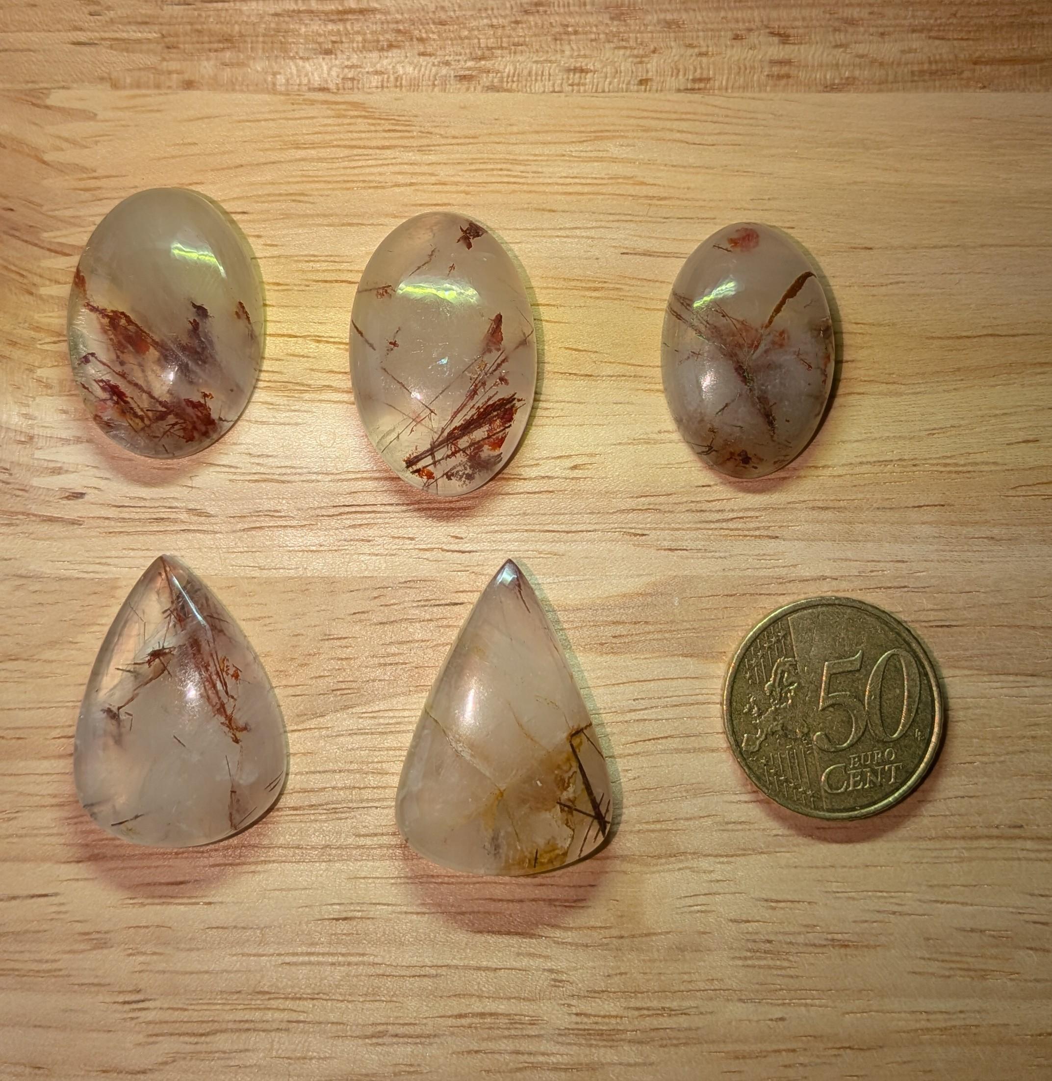 "Selectie Koper Rutielkwarts cabochons met roodbruine rutielnaalden in ovaal- en druppelvorm voor custom wire wrapped hangers, naast een 50 cent munt."