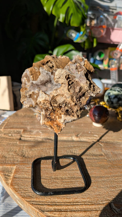 Voorzijde van een grillige kwartsgeode op zwarte standaard, rijk bezet met fonkelende witte kristallen.
