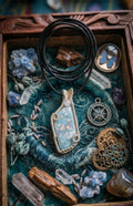 Handgemaakte blauw-witte Larimar hanger met verzilverd draadvlechtwerk, gepresenteerd in een houten kistje met steampunk tandwielen, kompas en kristallen.