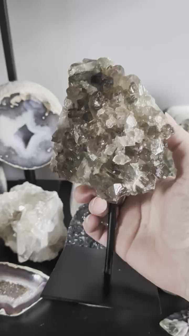 Een rookkwarts cluster van 890 gram op een zwarte standaard, met zicht op de diepe rokerige kristalstructuur