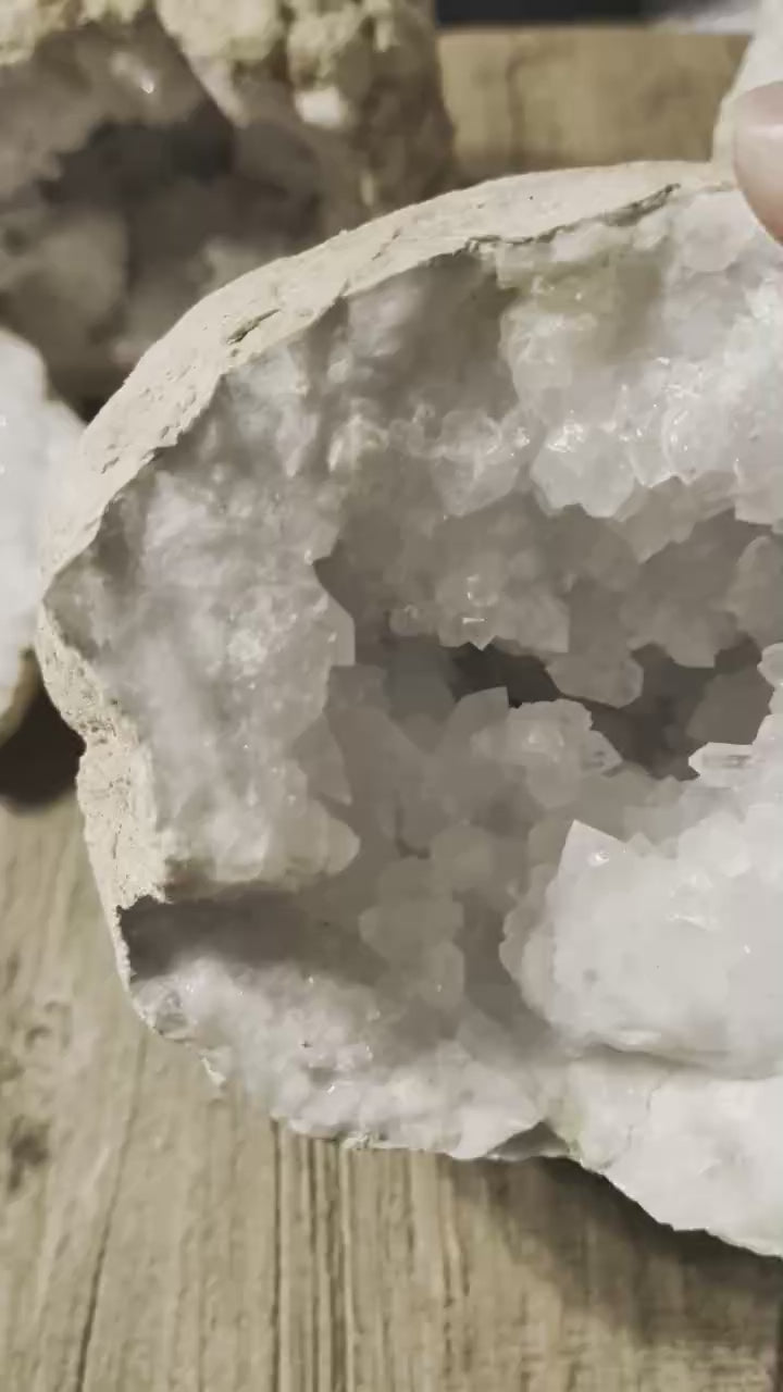 Grote massieve kristalgeode van 2,7 kilo met een diepe binnenzijde vol glinsterende witte kristallen, getoond op een houten achtergrond