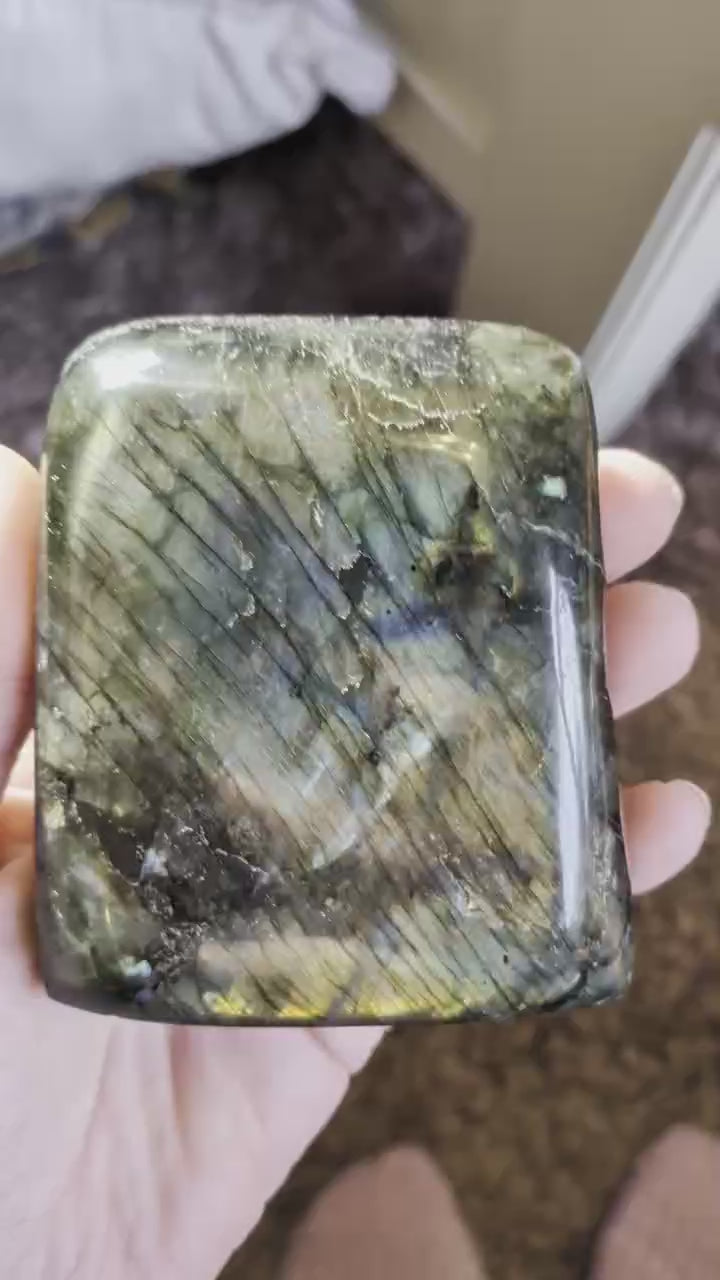 "Handgepolijste vrije vorm van Labradoriet met een intense blauwe en gouden glans, 9 cm hoog en 473 gram, getoond in een hand om de schittering te laten zien."