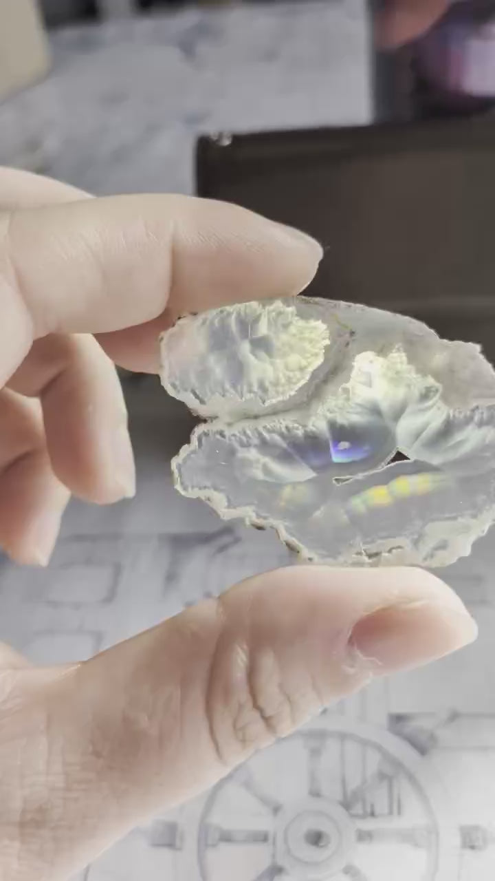 Video van een 5,5 cm Iris Agaat; bij beweging schieten felle iriserende banen van violet naar groen over de 2mm dikke kristalstructuur.