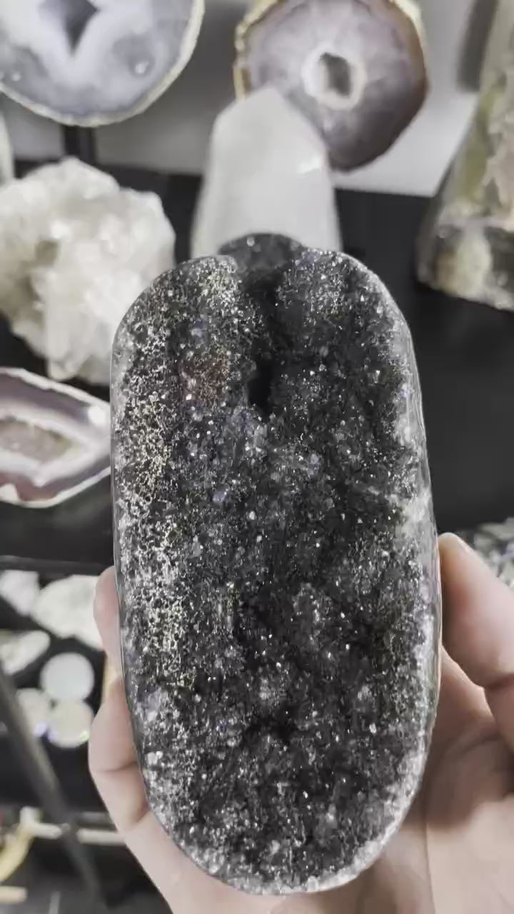 Een hand houdt een compacte zwarte Galaxy Amethist cluster van 370 gram vast, waarbij de glinsterende zwarte kristalstructuur goed zichtbaar is