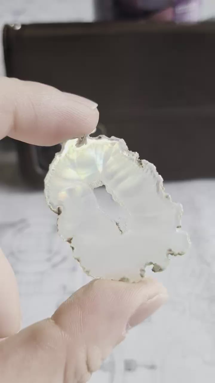 Video van een 4 cm Iris Agaat; bij beweging voor een lichtbron verschijnen er felle, geconcentreerde regenboogkleuren over de heldere 2mm dikke steen.