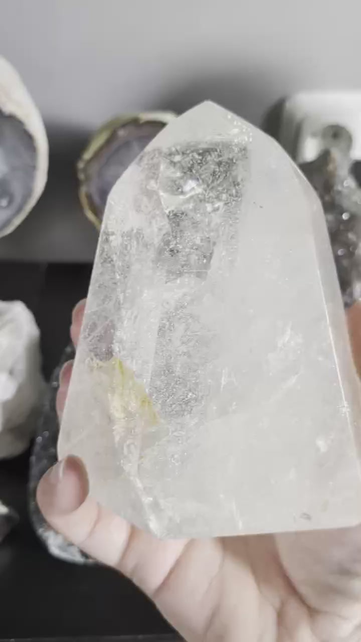 Een heldere, gepolijste bergkristal punt die staat op een houten ondergrond, met zichtbare natuurlijke insluitsels