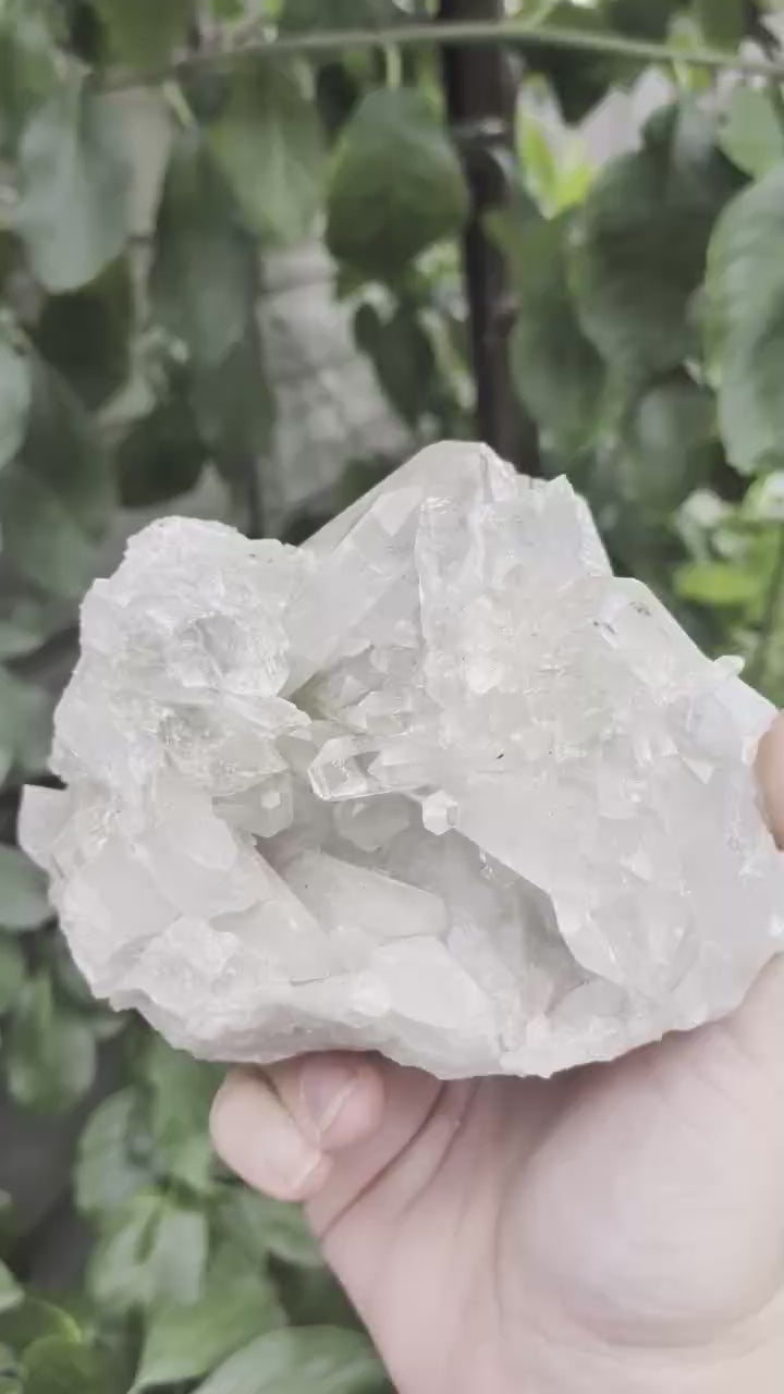 Een hand houdt een helder bergkristal cluster van 1163 gram vast, met zichtbare schitterende kristalpunten