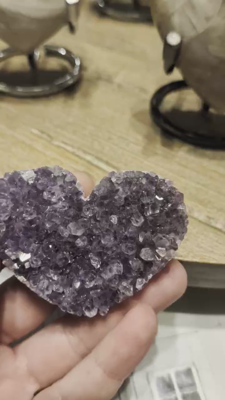 "Close-up van de sprankelende paarse kristalpunten in een klein handgeslepen amethist hart."