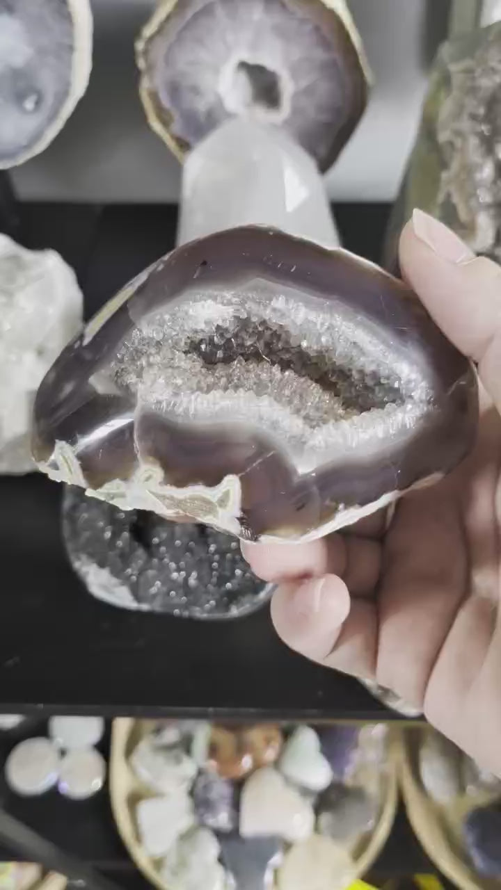 Een hand houdt een elegante Agaat-geode van 333 gram vast, met een diepe kleur en een schitterend kristalhart in het midden