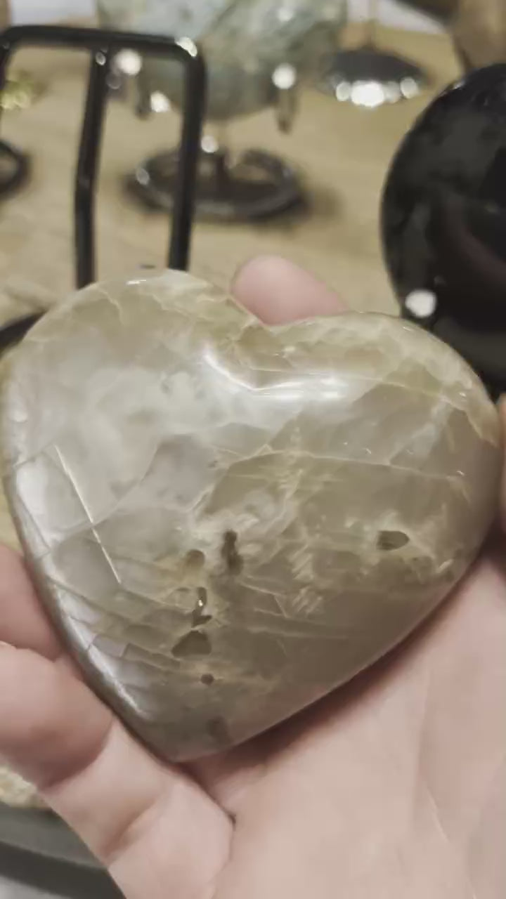 "Close-up van de prachtige zilveren glans en de gelaagde structuur van een gepolijst Grijze Maansteen hart."