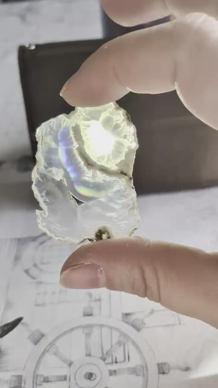 Video van een 5 cm Iris Agaat; bij het kantelen voor het licht schiet een felle, meebewegende regenboogflits over de 2mm dikke kristalstructuur.