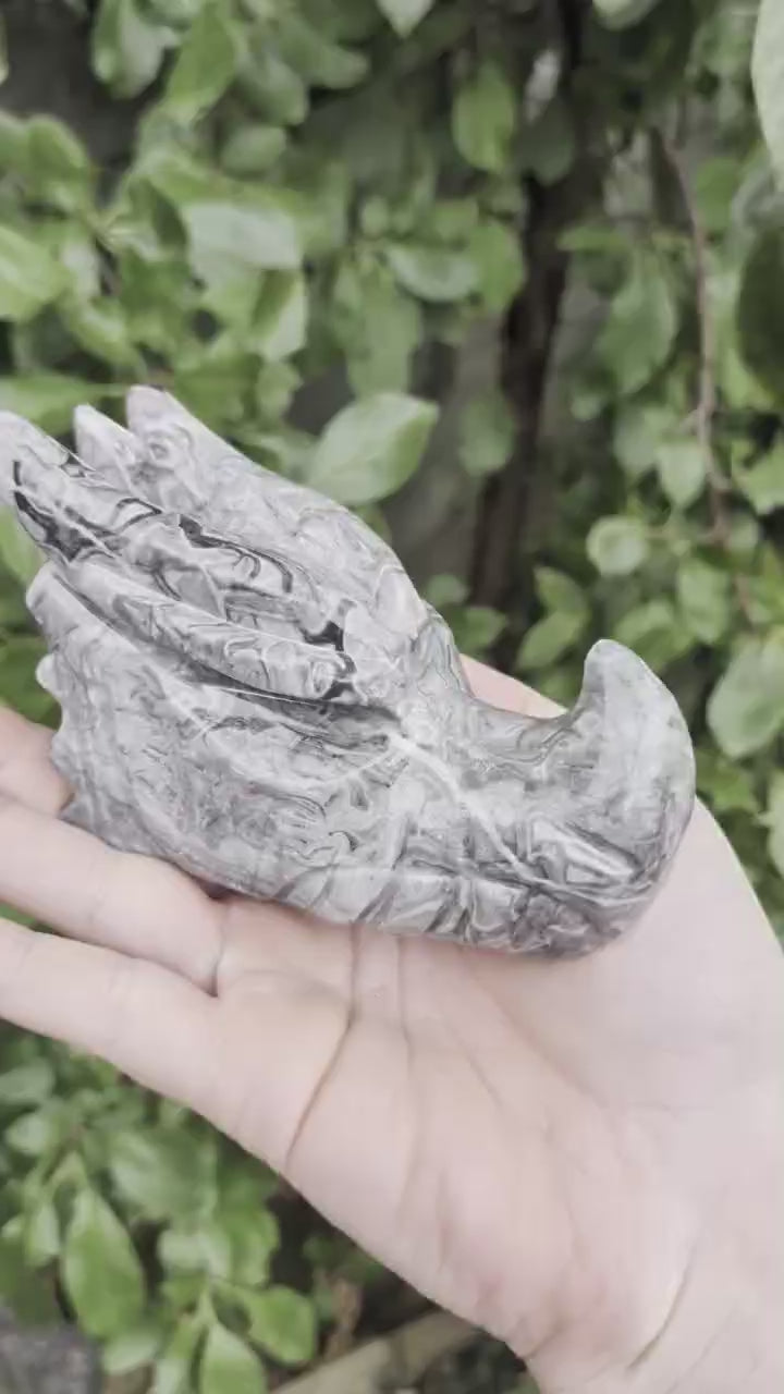 Gedetailleerde handgemaakte draken schedel van 439 gram in Picasso jaspis met grijze en zwarte patronen, vastgehouden in de hand.