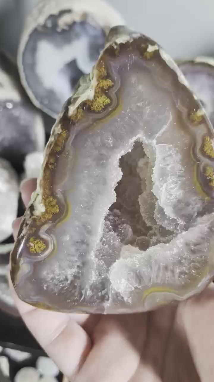 Een hand houdt een Agaat-geode van 500 gram vast met gelaagde aardetinten en een sprankelend kristalhart in het midden