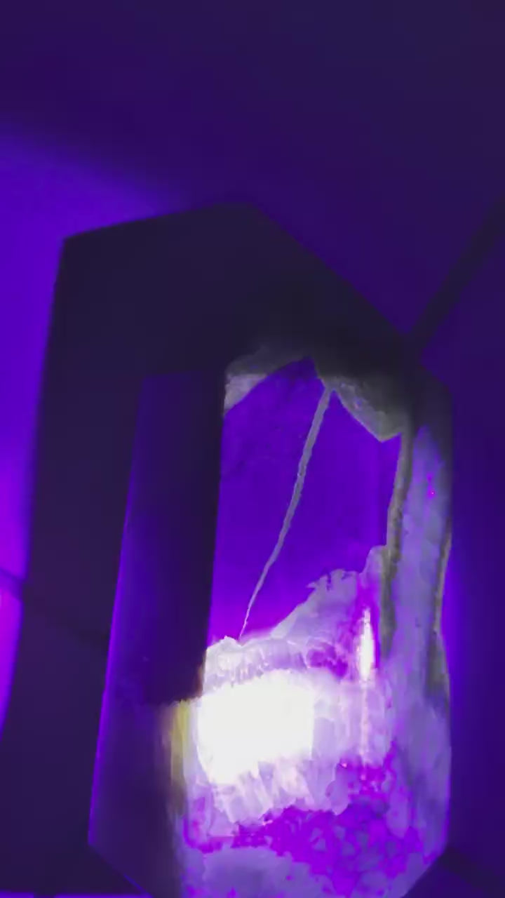 Septarie kristal toren die felgeel/groen oplicht onder een UV-lamp (blacklight).