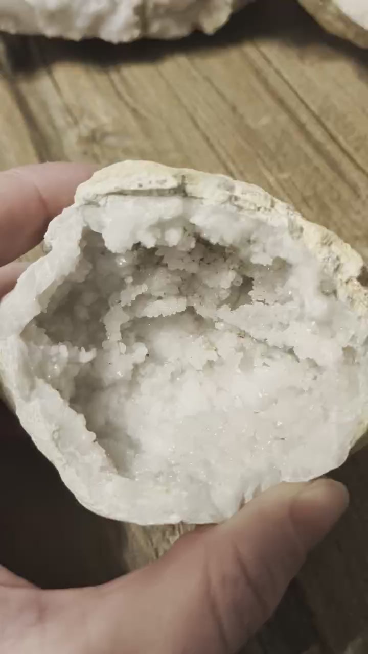 Opengewerkte witte kristalgeode met schitterende kristallen binnenin, liggend op een houten ondergrond.