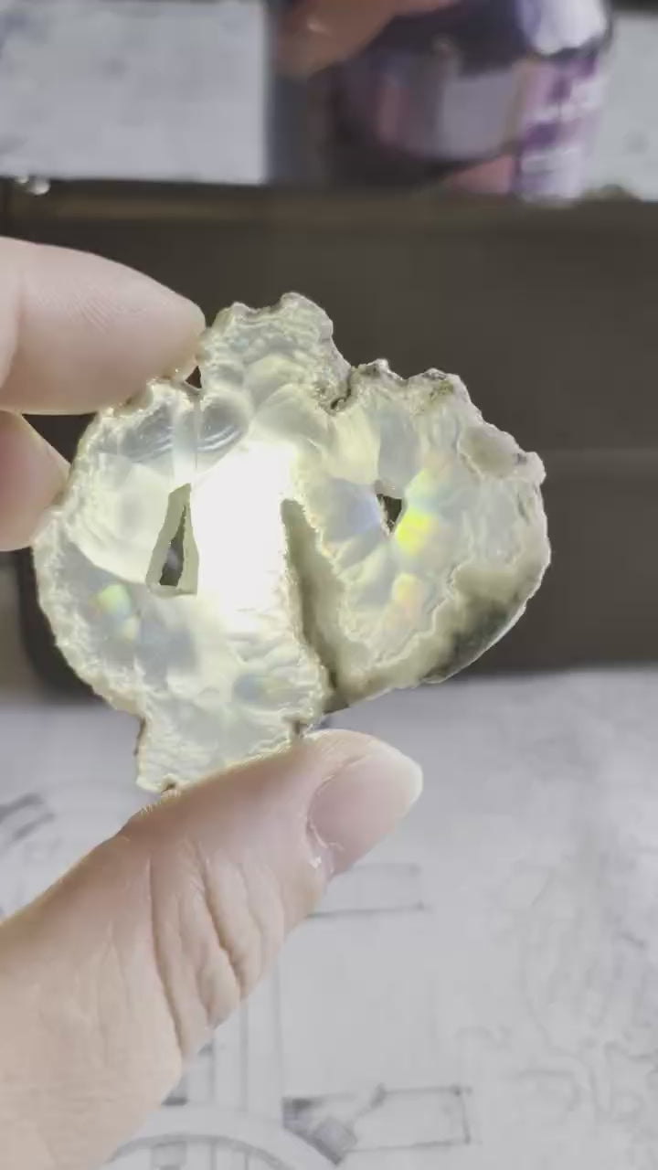 Video van een 5 cm Iris Agaat met dubbel venster; bij het kantelen voor een lichtbron verschuiven felle regenboogkleuren over de 2mm dikke steen.