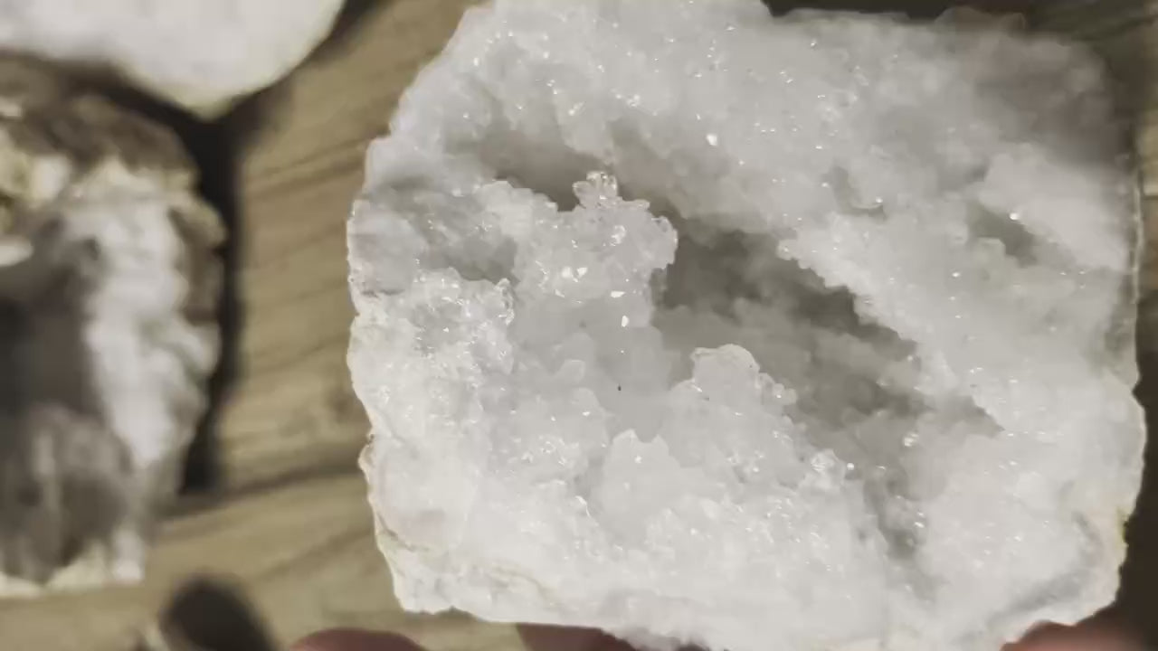 Grote opengebroken kristalgeode van 400 gram met witte glinsterende kristallen, gefotografeerd op een rustieke houten tafel.