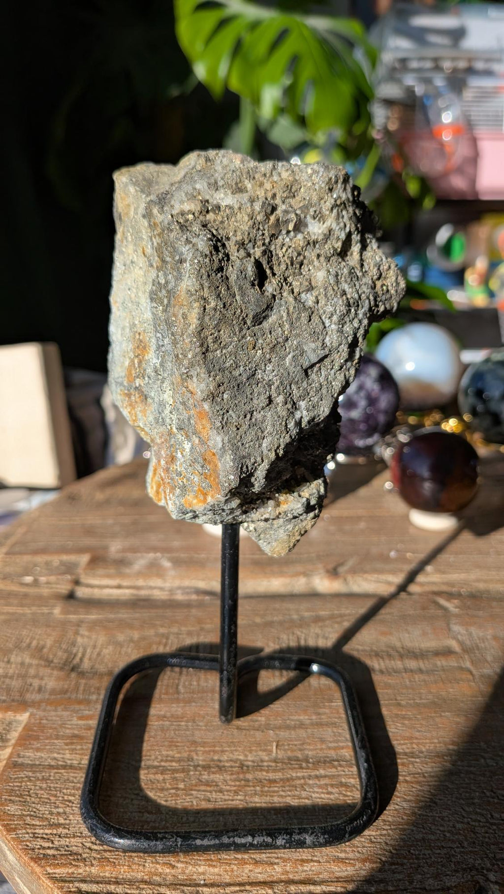 Ruwe pyriet edelsteen op een zwarte standaard, tonend een metallic grijze en goudachtige glans met een hoekige kristalstructuur.