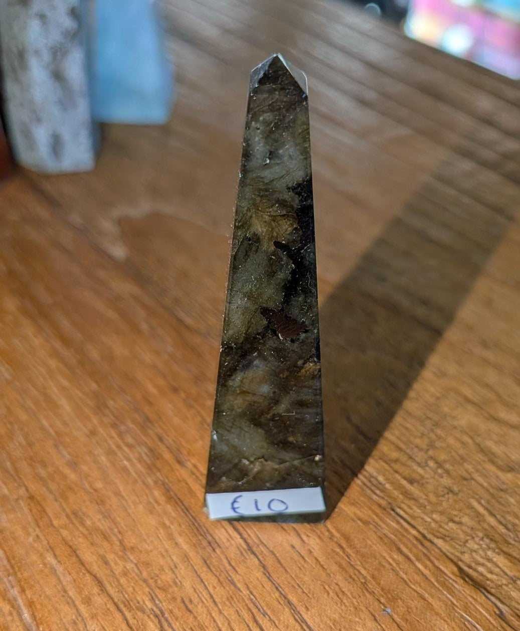 "Slanke gepolijste labradoriet toren van 6,5 cm met een opvallende blauwe en gouden glans, vastgehouden in een hand tegen een houten achtergrond."