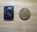 Gefacetteerde rechthoekige Sodaliet edelsteen met donkerblauwe en grijze patronen naast een munt ter schaalvergelijking.