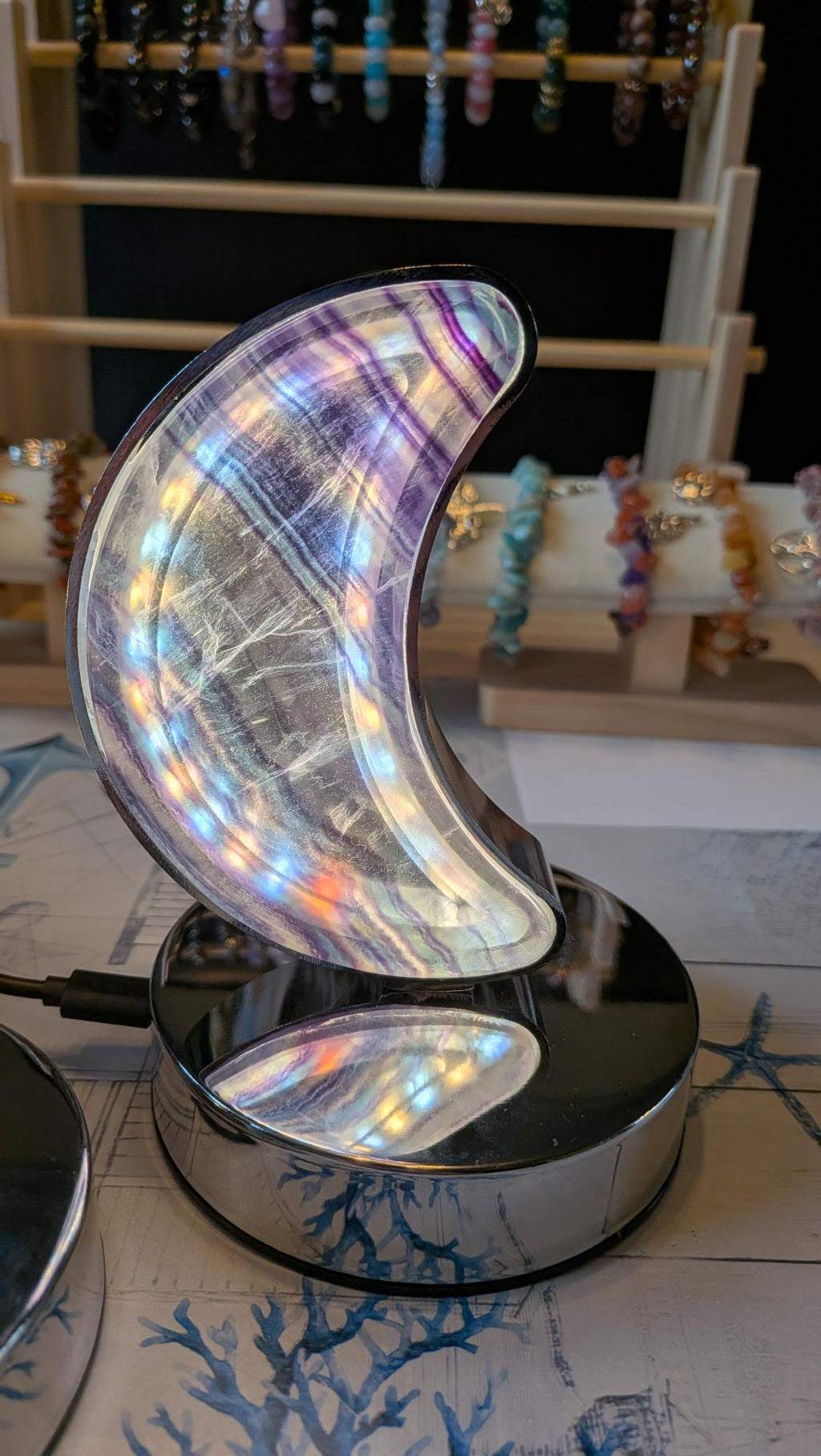 Luxe edelsteen lamp van Regenboog Fluoriet in de vorm van een halve maan met paarse en groene banden, brandend op een chromen voet.