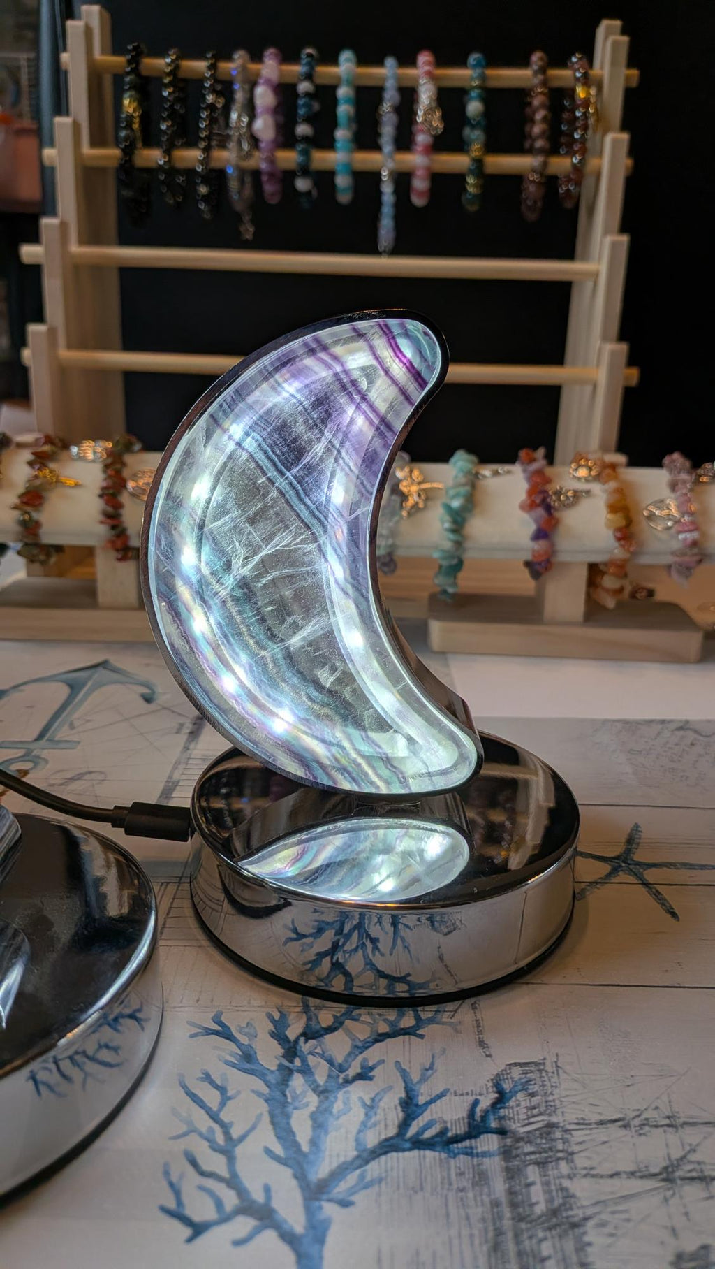 Luxe edelsteen lamp van Regenboog Fluoriet in de vorm van een halve maan met paarse en groene banden, brandend op een chromen voet.