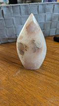 Gepolijste punt van Bloemagaat met zachte roze en witte patronen op een houten ondergrond, 10 cm hoog en 245 gram.